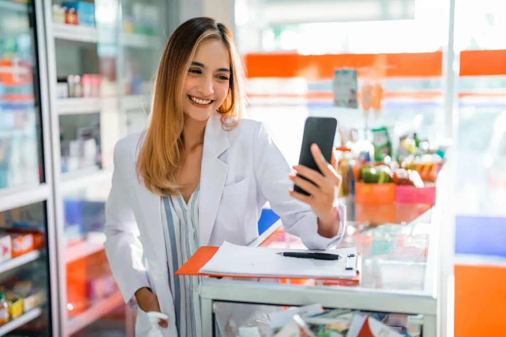 Foto ilustrativa de farmacêutica com celular. Aprenda estratégias de marketing local para farmácias clínicas.