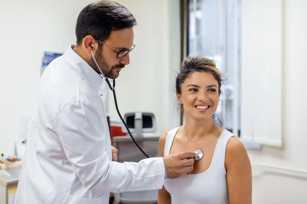 Foto de profissional de saúde ouvindo coração da paciente. Check-up cardiovascular pode ser feito na farmácia clínica.